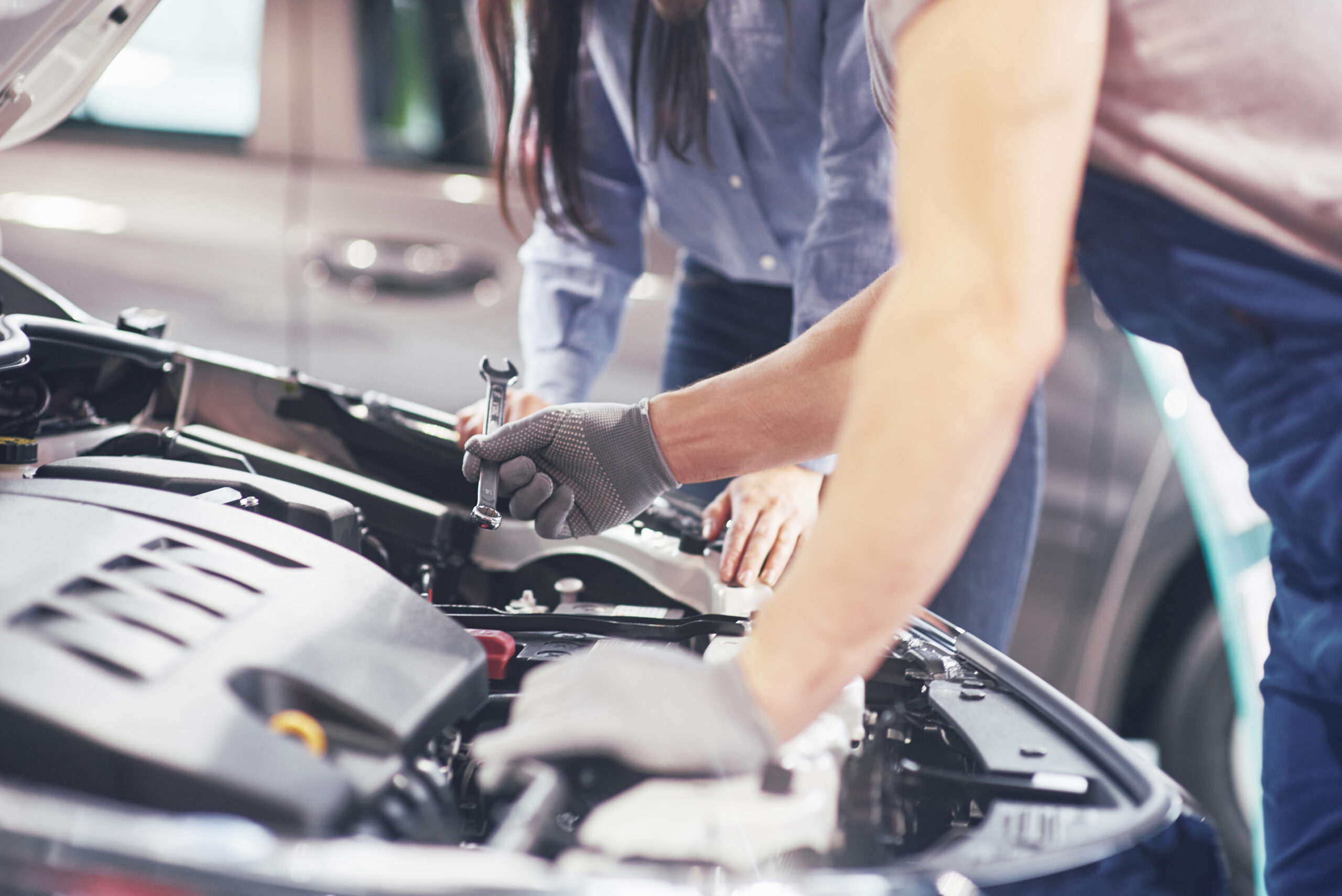 A man mechanic and woman customer look at the car hood and discuss repairs.